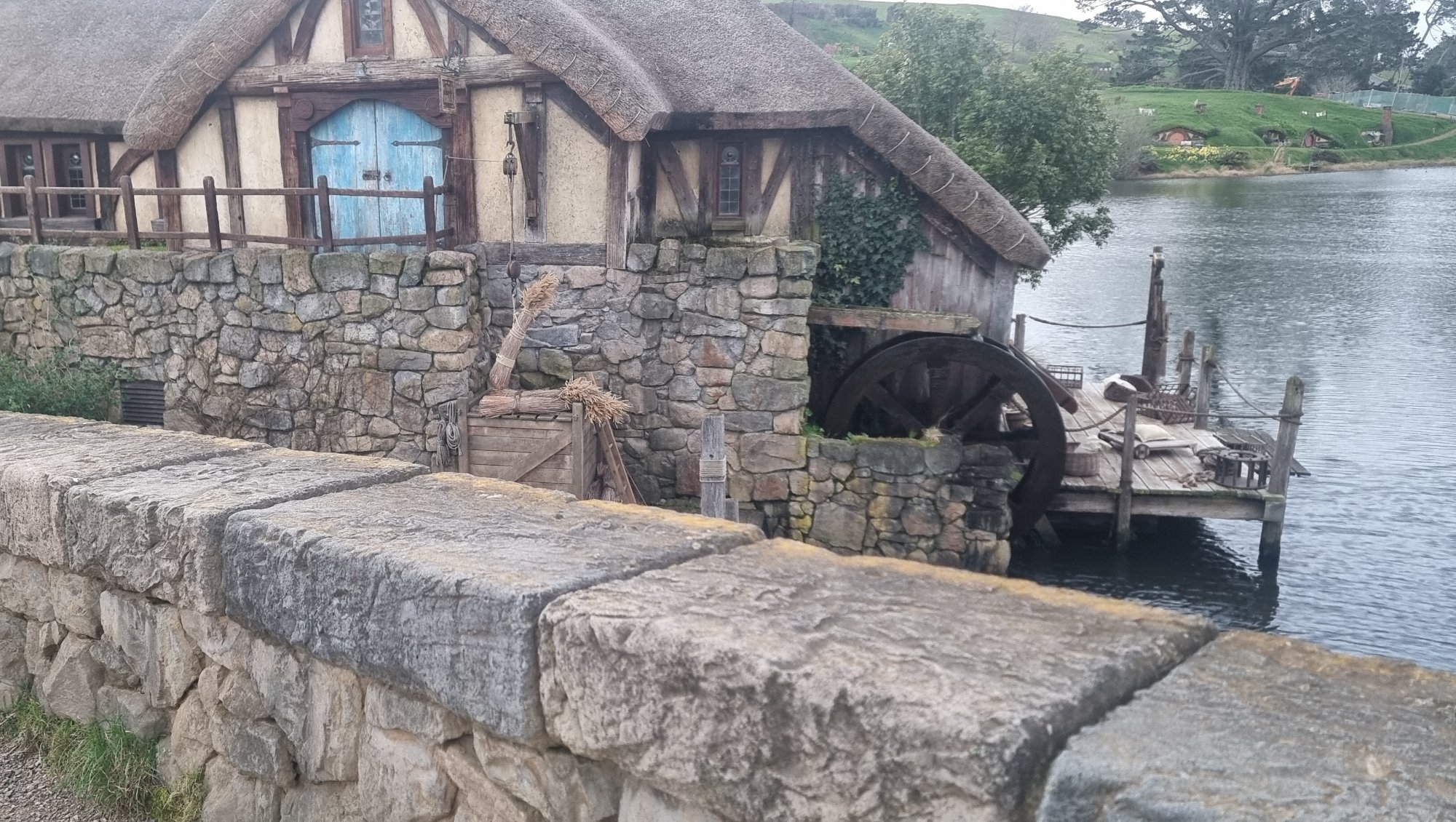 The Mill and waterwheel at Hobbiton Movie Set with the lake and double-arch bridge